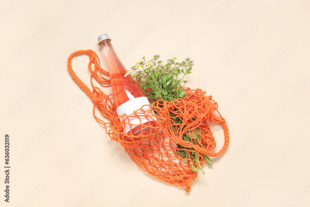 Mesh bag with beautiful chamomile flowers and bottle of juice on beige background