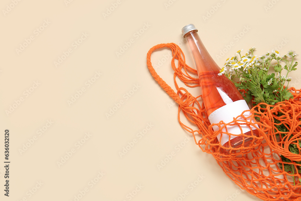 Mesh bag with beautiful chamomile flowers and bottle of juice on beige background