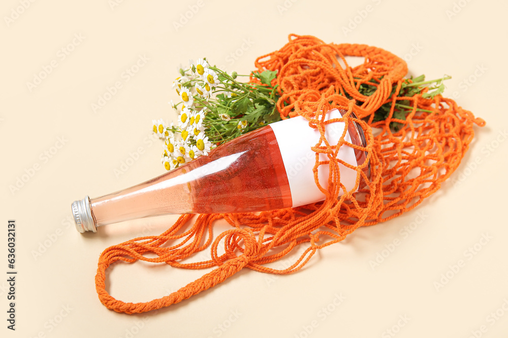 Mesh bag with beautiful chamomile flowers and bottle of juice on beige background, closeup