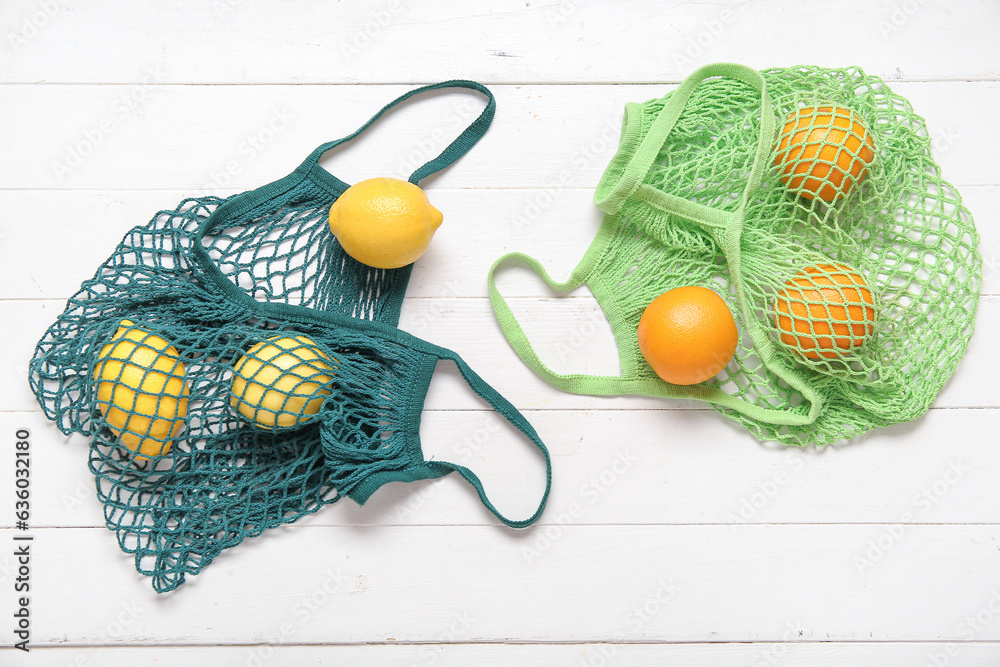 Mesh bags with fresh lemons and oranges on light wooden background