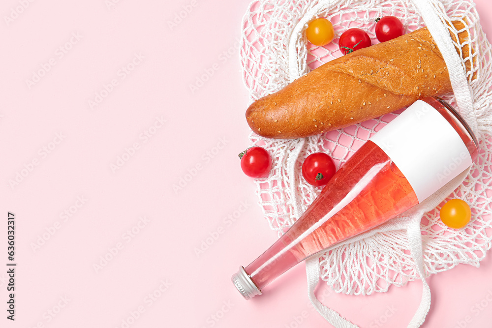 Mesh bag with fresh tomatoes, baguette and bottle of juice on pink background, closeup