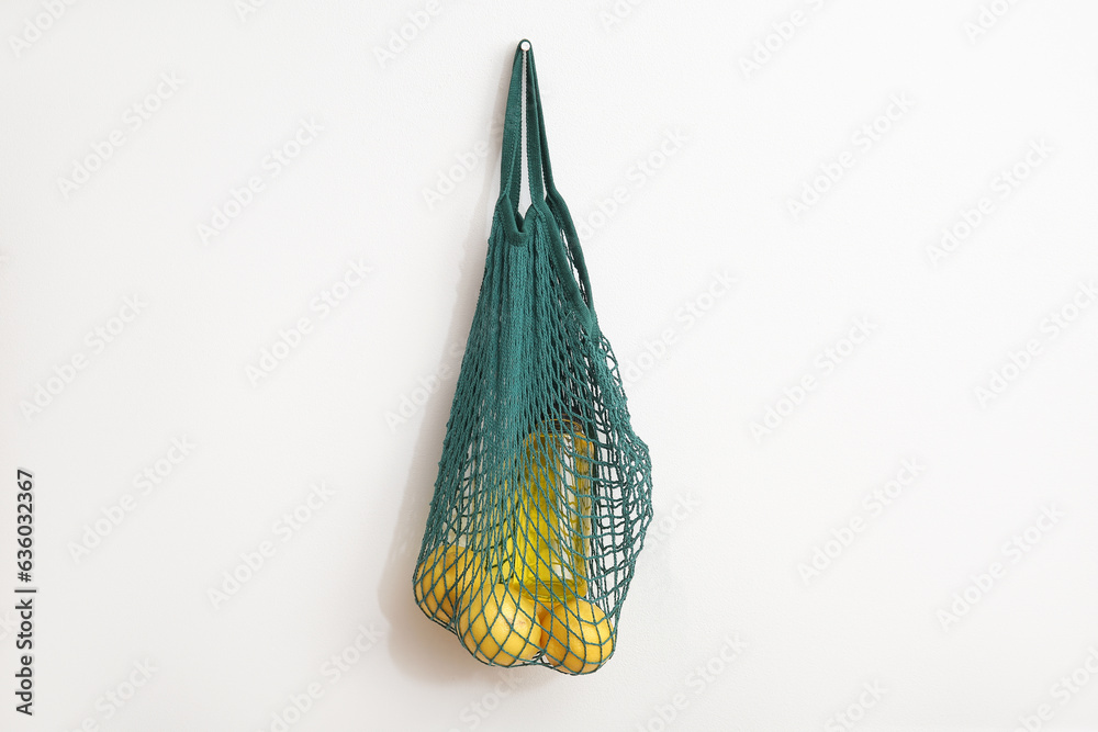 Mesh bag with fresh lemons hanging on light wall in room