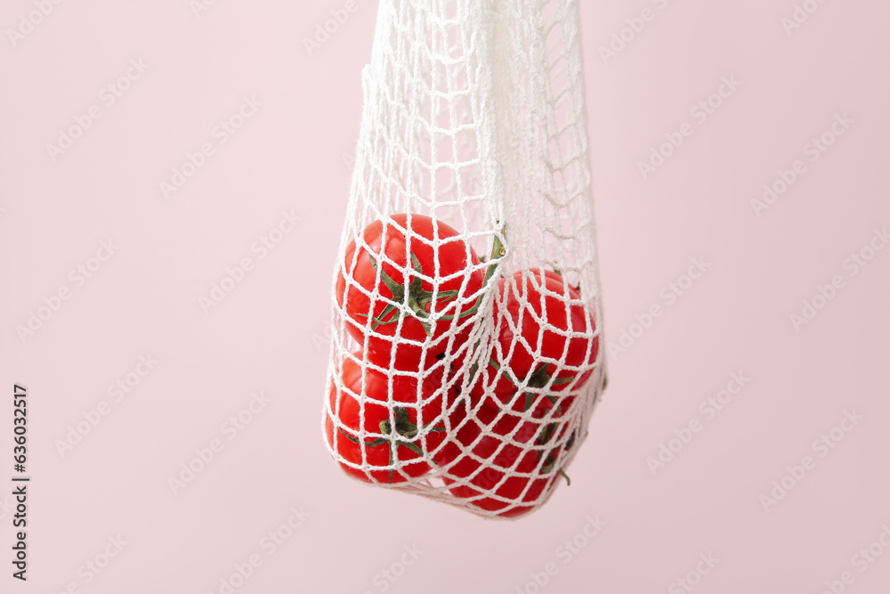 Mesh bag with fresh tomatoes on beige background, closeup