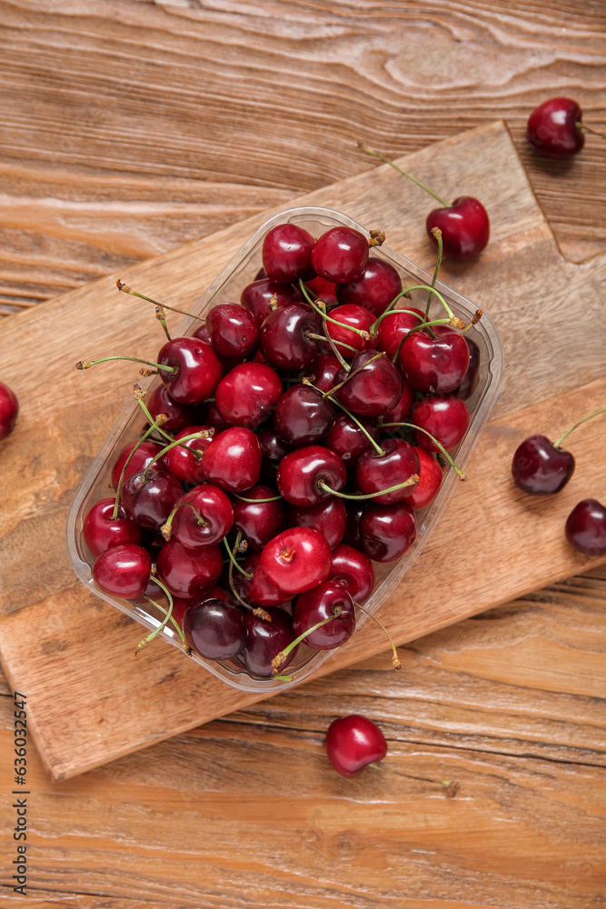 Plastic container with fresh cherry on wooden background