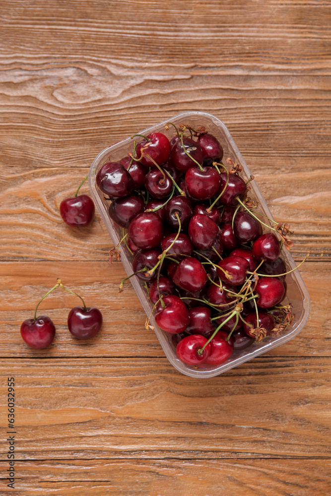 Plastic container with fresh cherry on wooden background