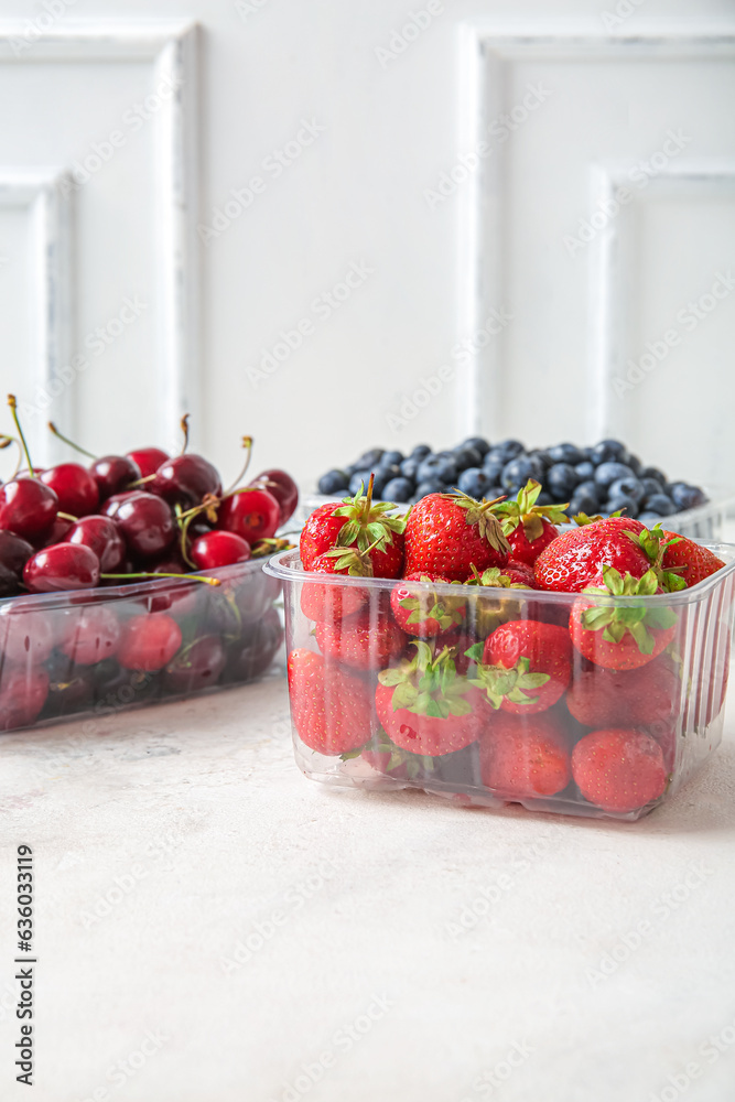 Plastic containers with fresh cherry and strawberry on light background, closeup