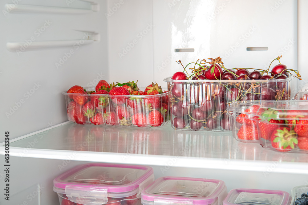 Plastic containers with fresh berries in refrigerator