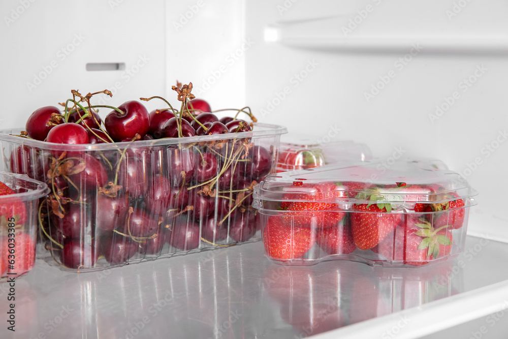 Plastic containers with fresh cherry and strawberry in refrigerator, closeup