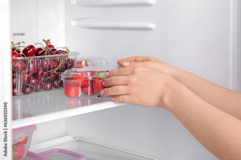 Female hands and plastic containers with fresh strawberry in refrigerator, closeup