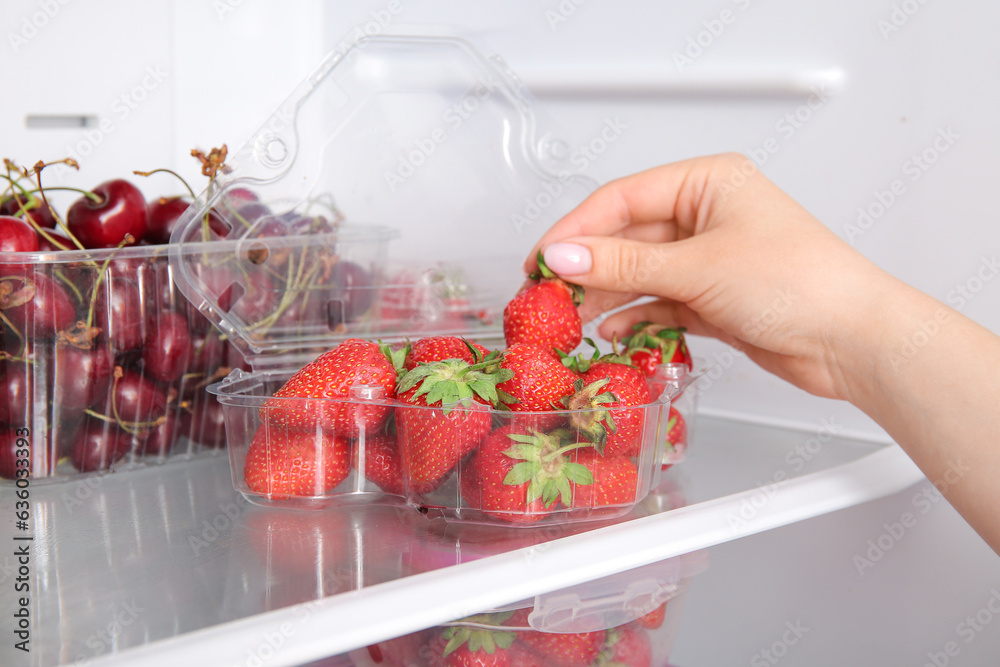 Woman taking strawberry in plastic container from refrigerator, closeup