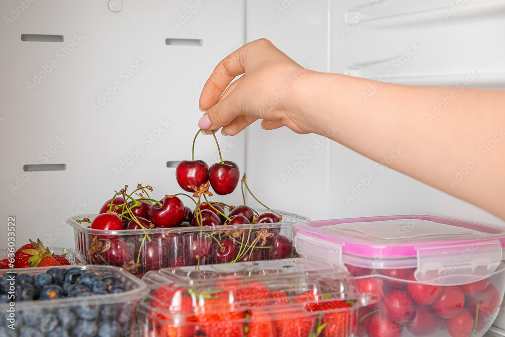 Woman taking cherry in plastic container from refrigerator, closeup