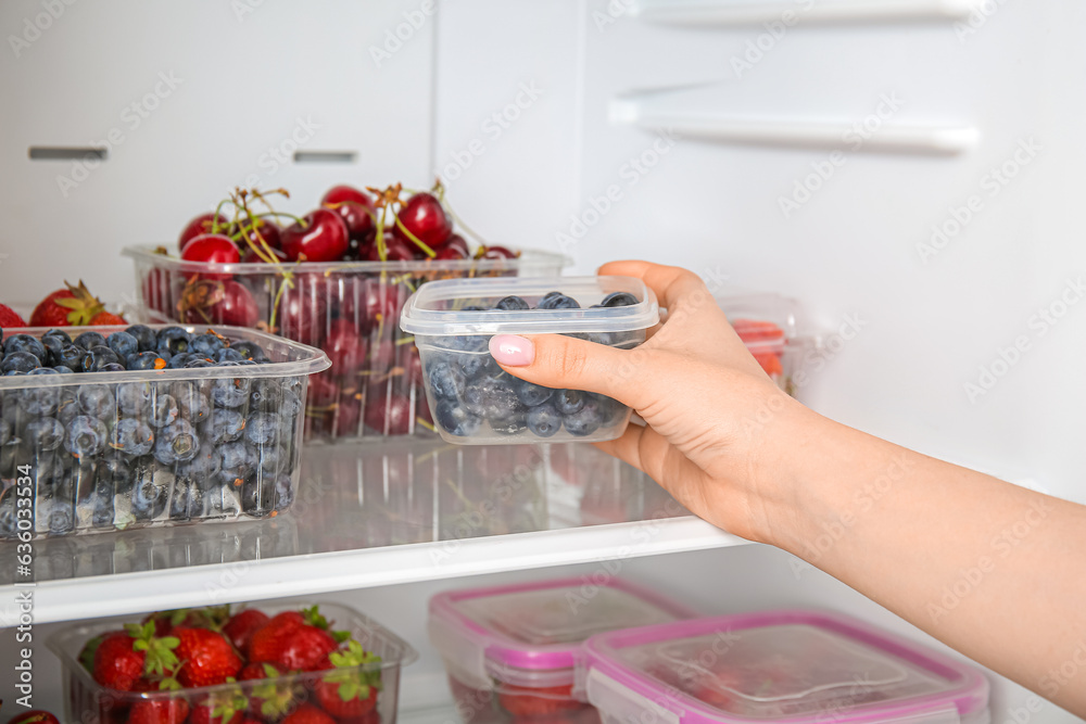 Woman taking blueberry in plastic container from refrigerator, closeup