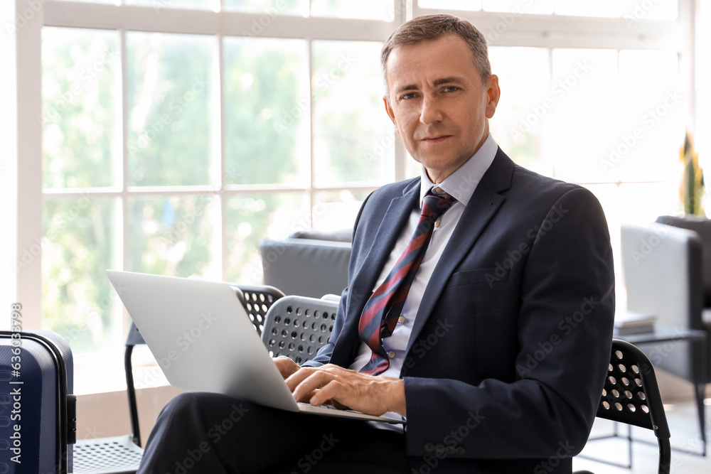 Mature businessman using laptop in hall of airport