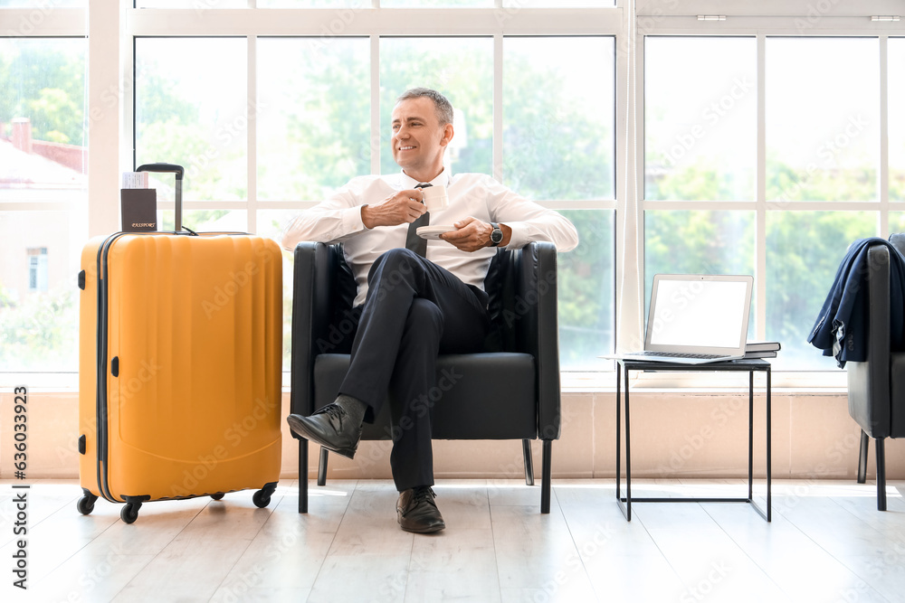 Mature businessman with cup of coffee sitting in hall of airport