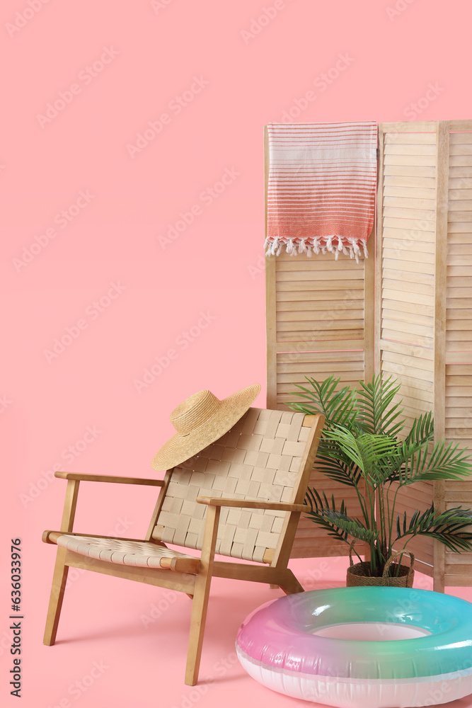 Chair with inflatable ring, wicker hat and folding screen on pink background. Travel concept