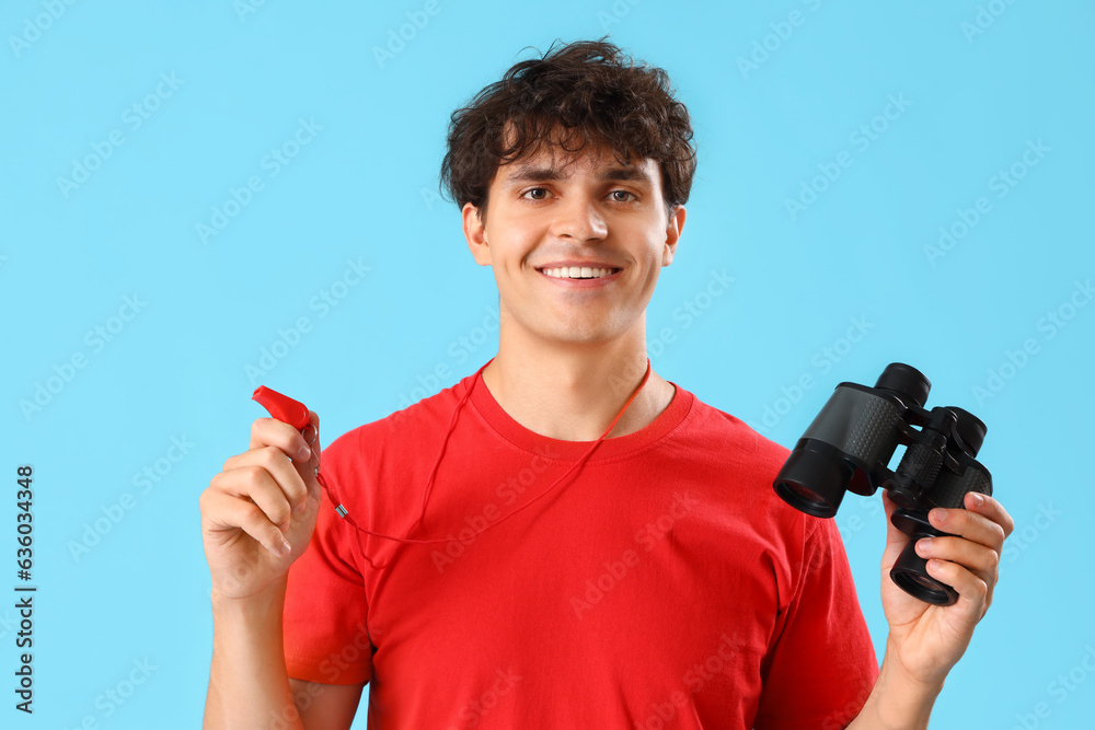 Male lifeguard with binoculars and whistle on blue background