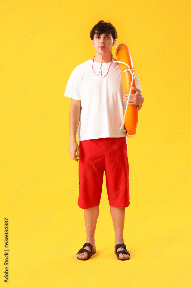 Male lifeguard with ring buoy whistling on yellow background