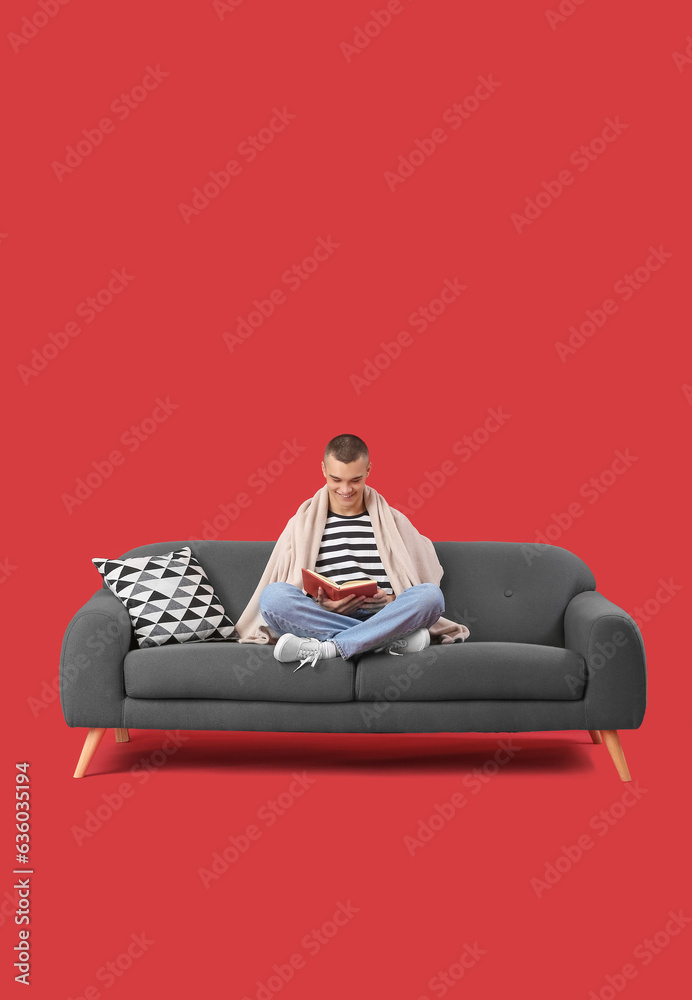 Happy young man sitting on sofa and reading book against red background