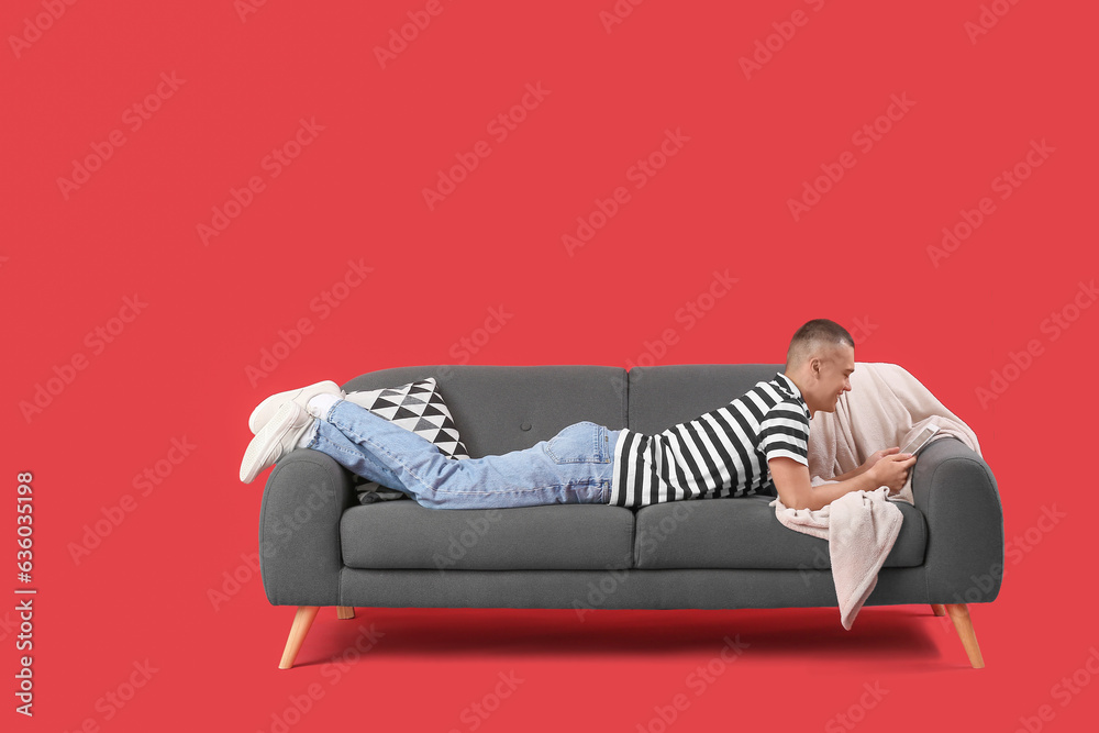 Happy young man lying on sofa and reading book against red background