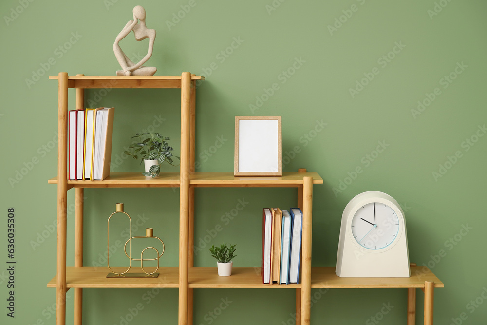 Shelving unit with books, clock and blank frame near green wall in room