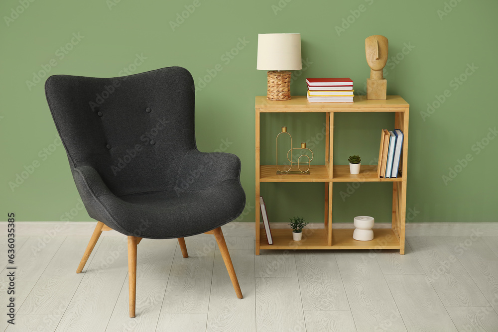 Shelving unit with books, decor and armchair near green wall in room