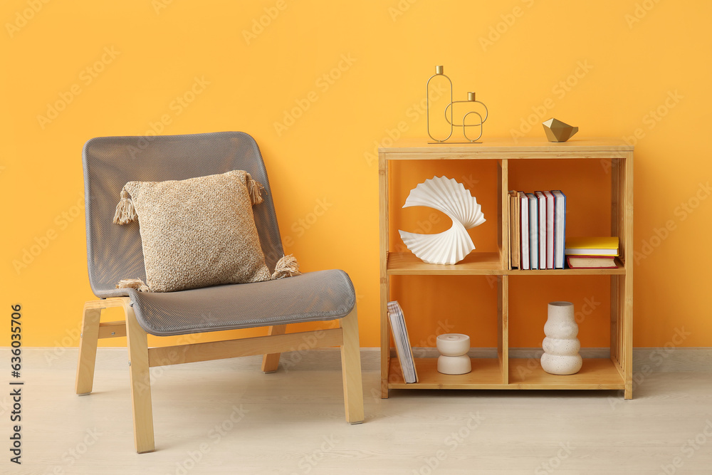 Shelving unit with books, decor and chair near orange wall in room