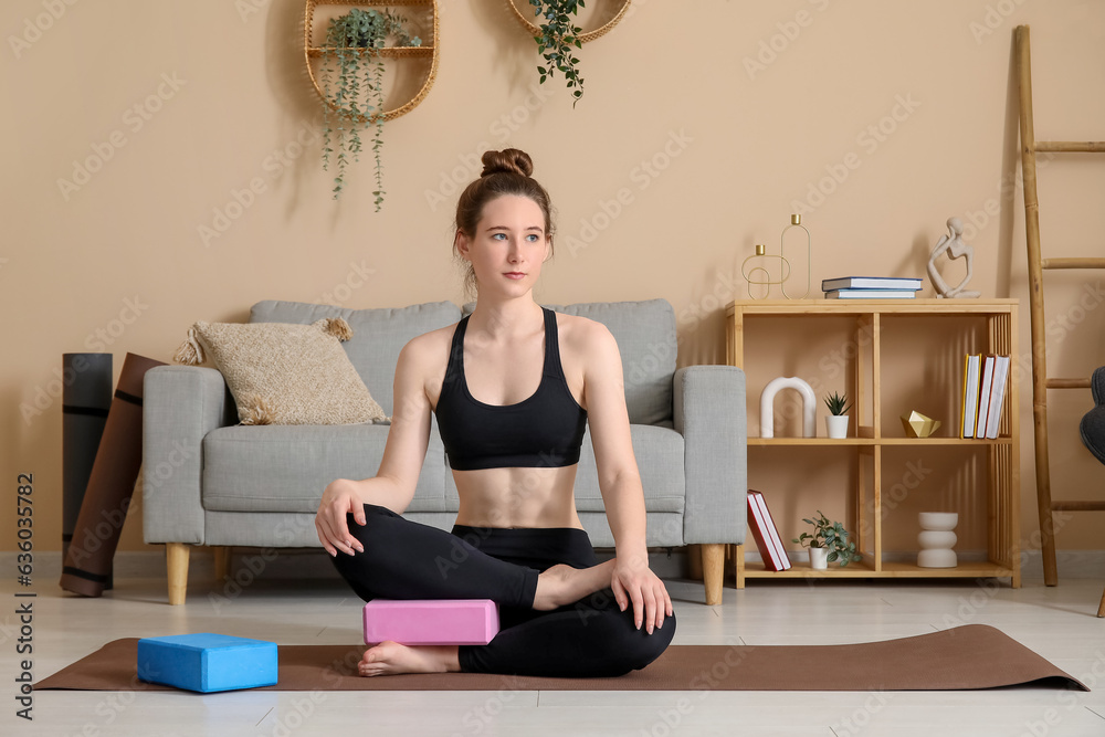 Sporty young woman practicing yoga with block at home