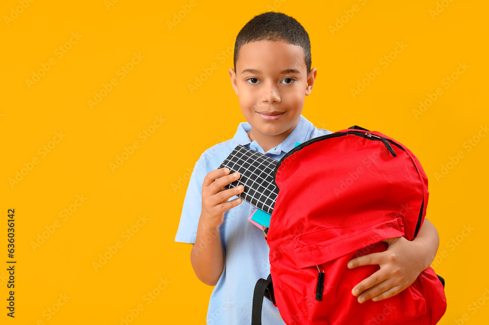 Little African-American schoolboy with pencil case and backpack on orange background