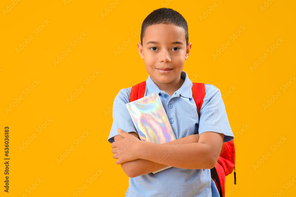 Little African-American schoolboy with pencil case on orange background