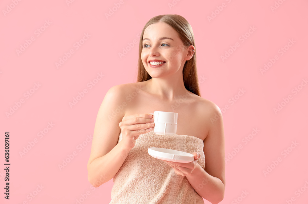 Pretty young woman wrapped in towel drinking coffee on pink background