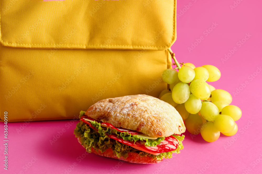 Lunch box bag with sandwich and grapes on pink background