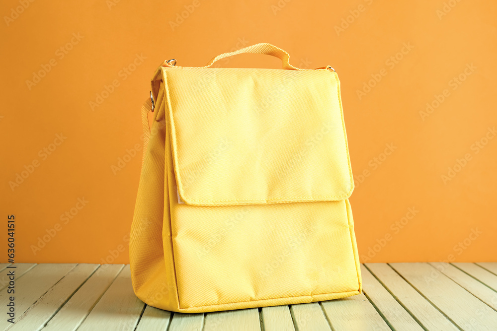 Yellow lunch box bag on green wooden table near orange wall