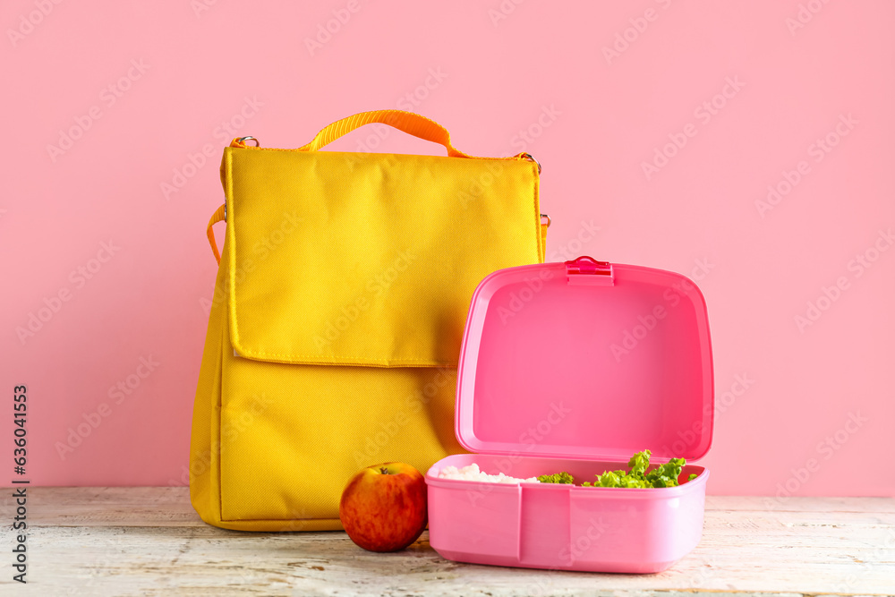 Bag and lunchbox with tasty food on white wooden table near pink wall