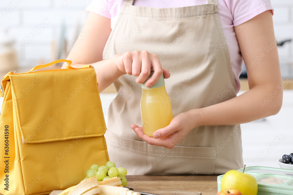 Woman packing bottle of juice into lunch box bag in kitchen