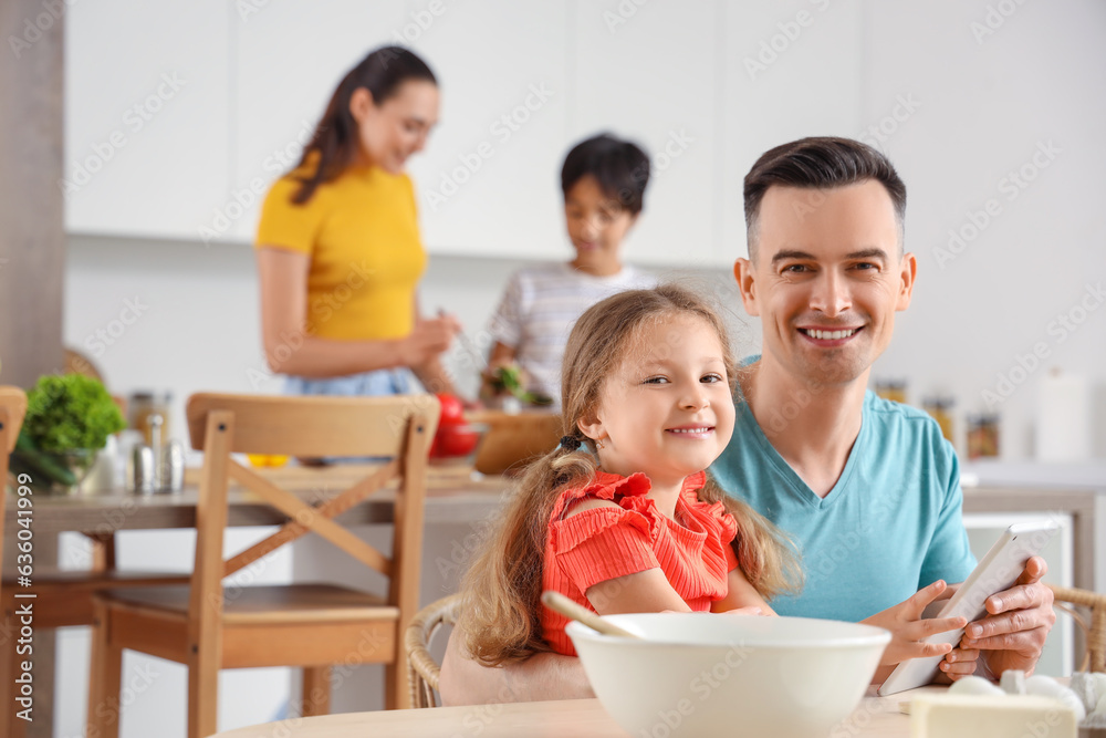 Little girl with her father using tablet computer in kitchen