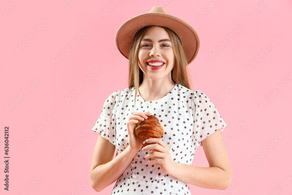 Beautiful young woman in wicker hat with tasty croissant on pink background