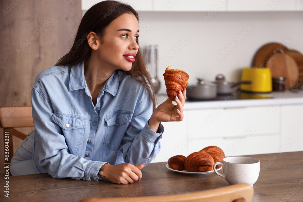 Beautiful young woman with tasty croissants and cup of coffee in kitchen