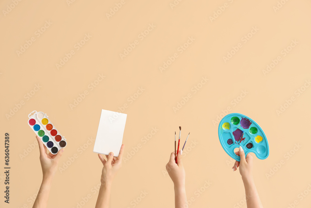 Female hands holding painting supplies on beige background