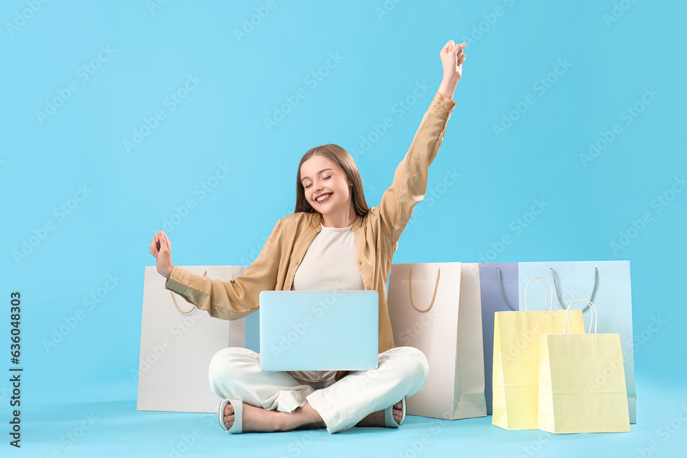 Pretty young woman with laptop and shopping bags on blue background. Online shopping concept