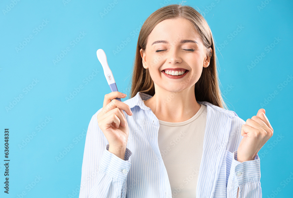 Happy young woman with positive pregnancy test on blue background