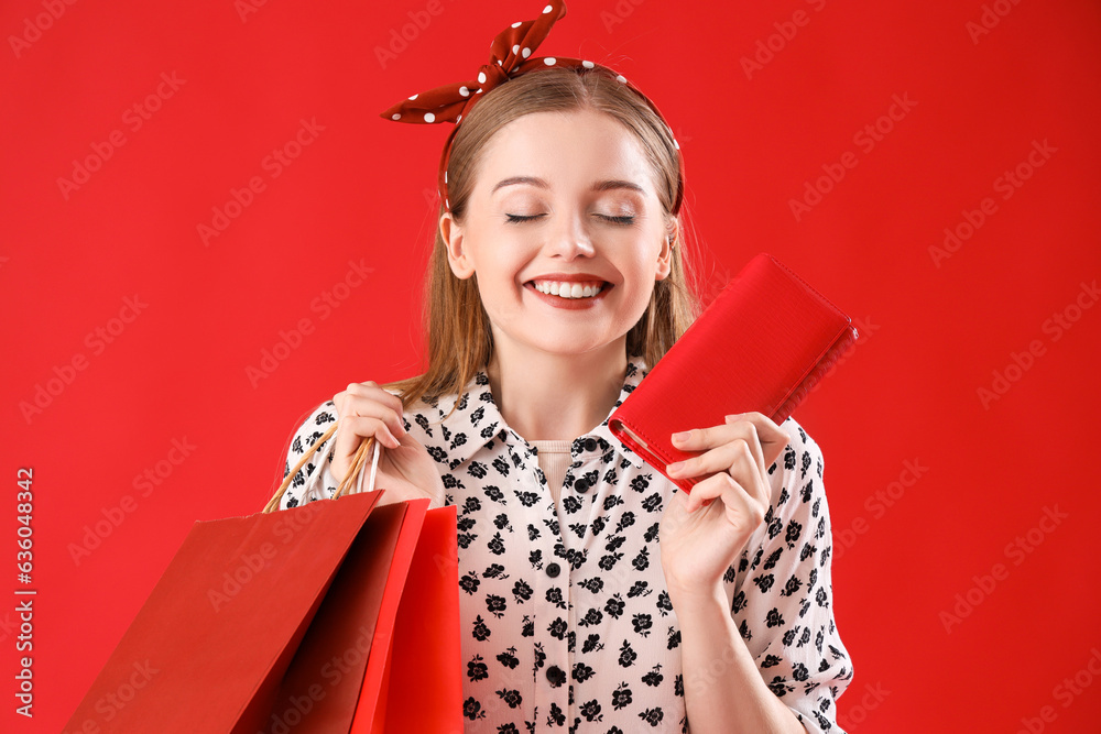 Happy young woman with shopping bags and purse on red background