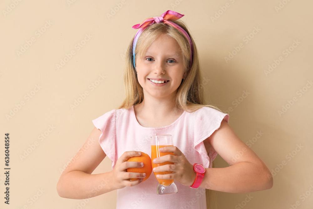 Little girl with glass of juice and orange on beige background