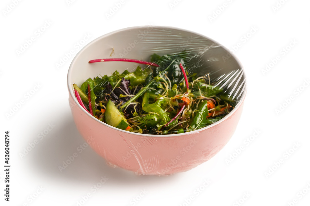 Bowl of fresh salad covered with plastic food wrap on white background