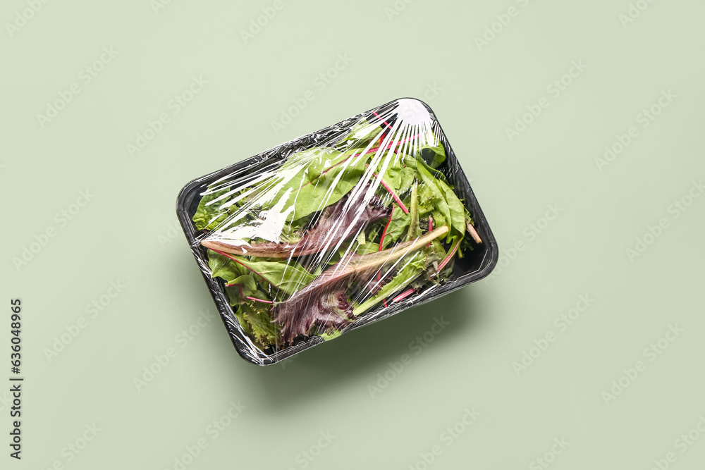 Fresh salad leaves covered with plastic food wrap on green background