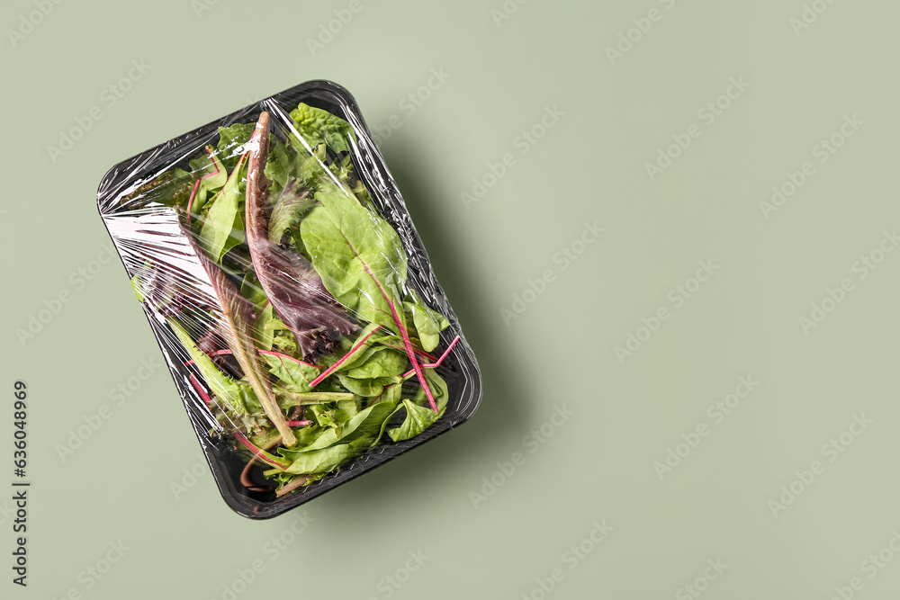 Fresh salad leaves covered with plastic food wrap on green background