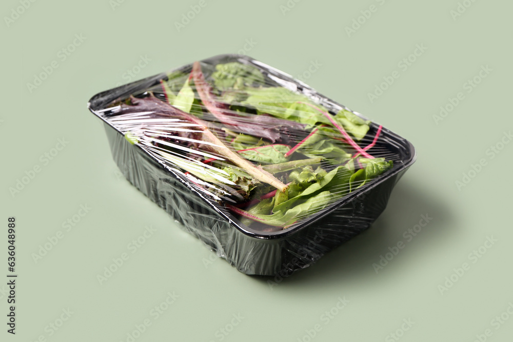 Fresh salad leaves covered with plastic food wrap on green background