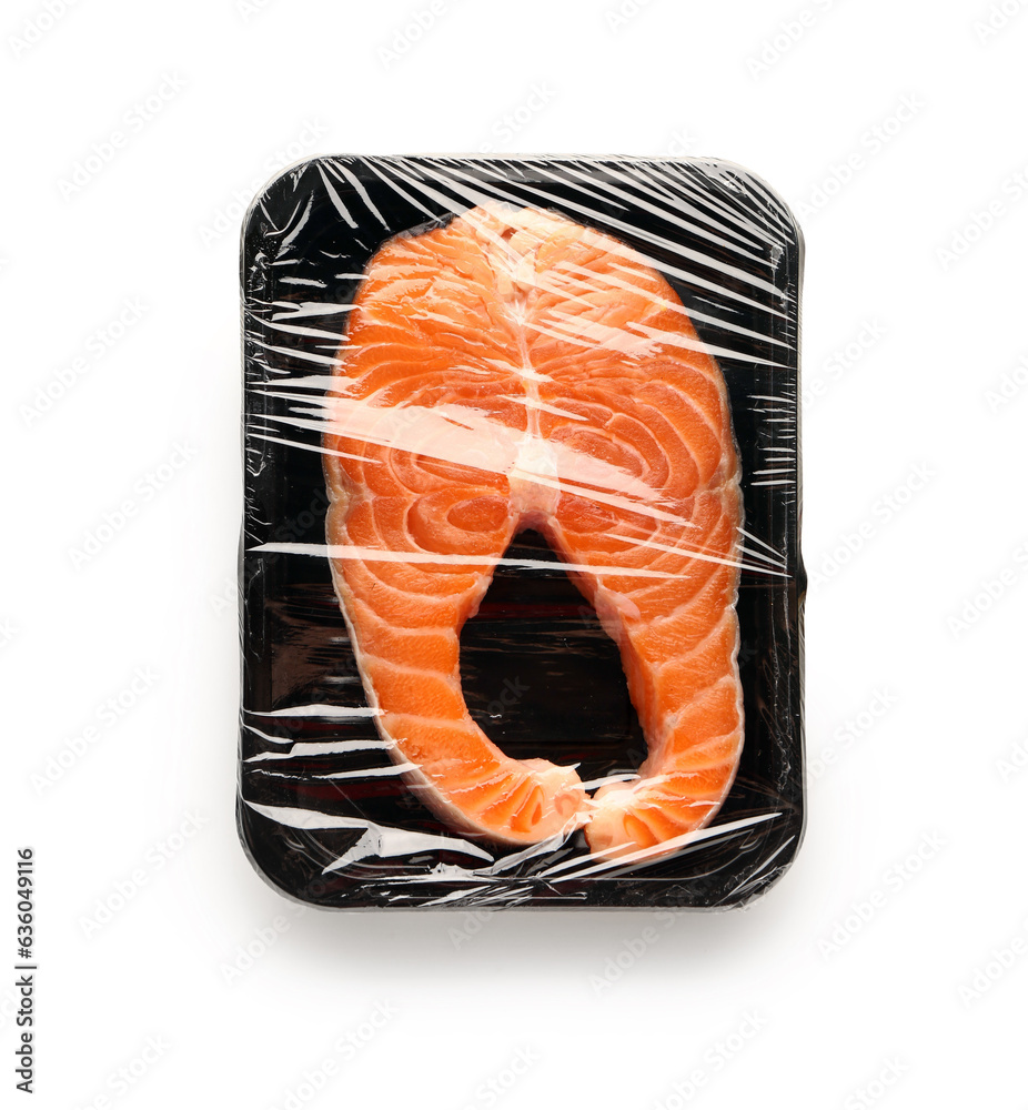 Fresh salmon steak in plastic food wrap on white background