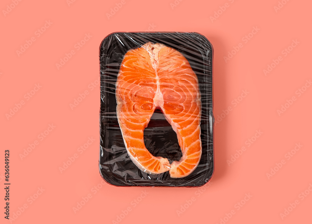 Fresh salmon steak in plastic food wrap on pink background