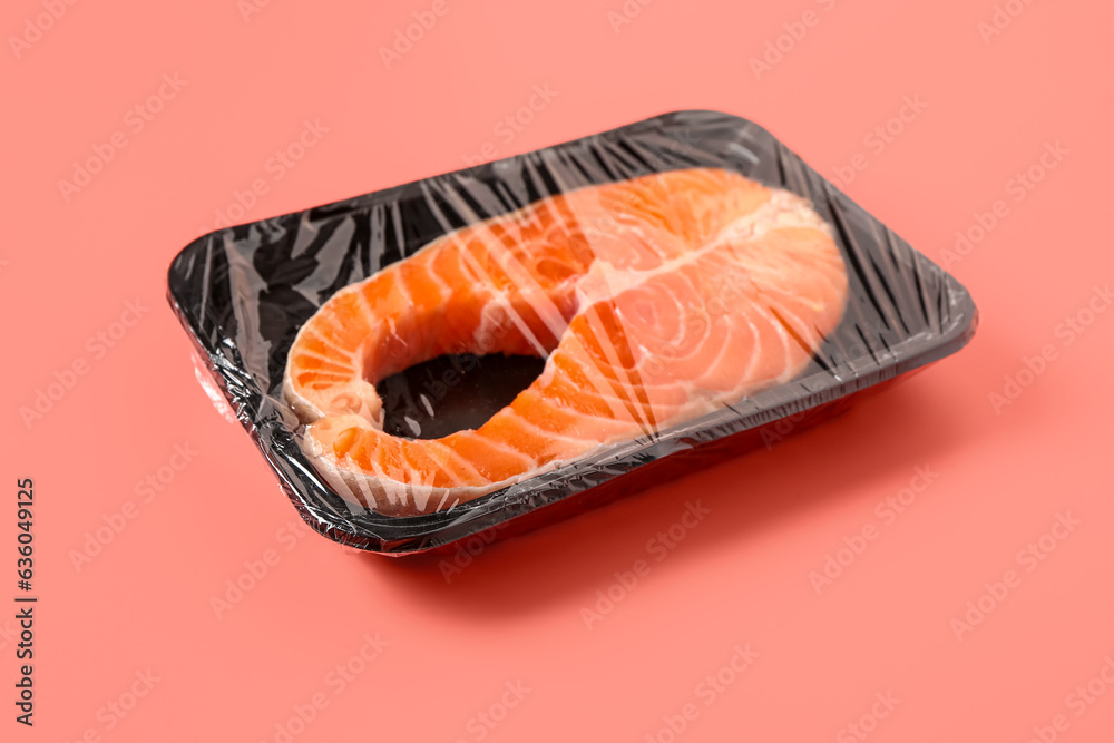 Fresh salmon steak in plastic food wrap on pink background