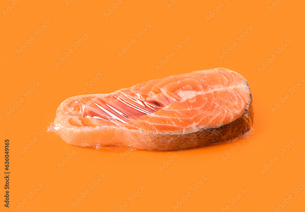 Fresh salmon steak in plastic food wrap on orange background